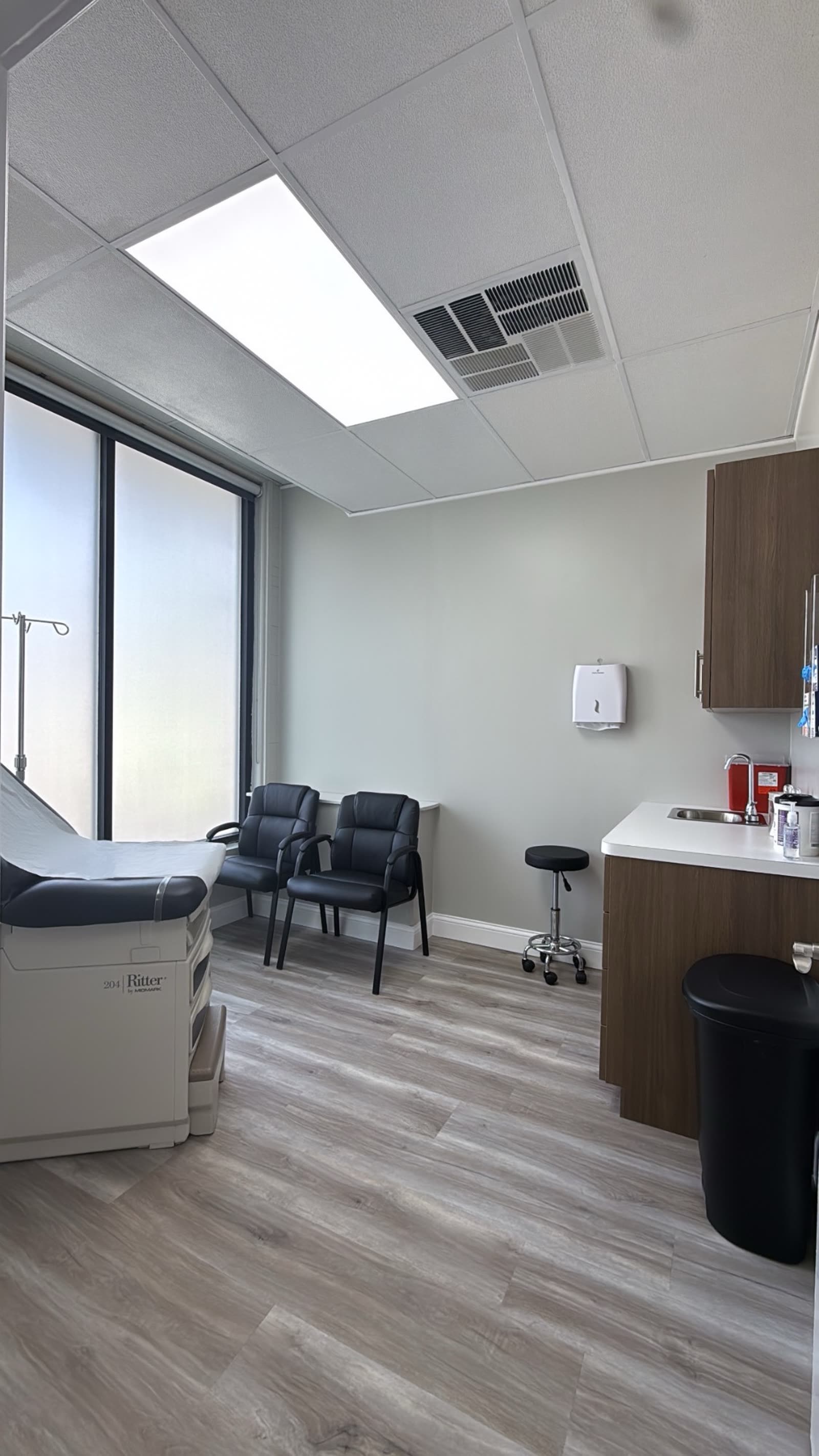 An exam room at Monarch Urgent Care with an exam table, seating and a clinical sink
